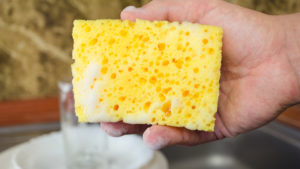 Man for hand holding a sponge to wash dishes with foam at the kitchen close up